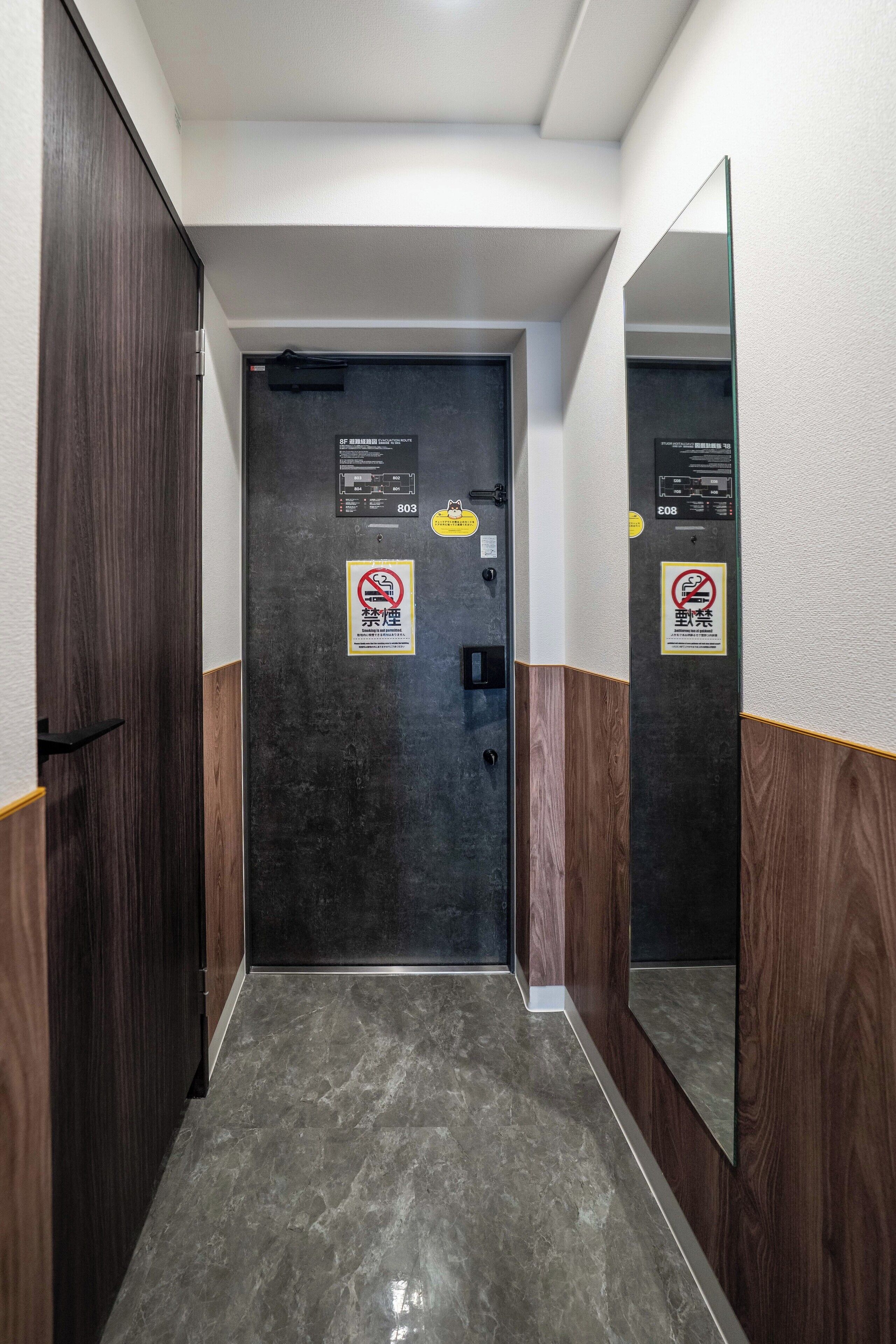 A narrow hallway with a dark door, wooden walls, and a mirror reflecting the door.