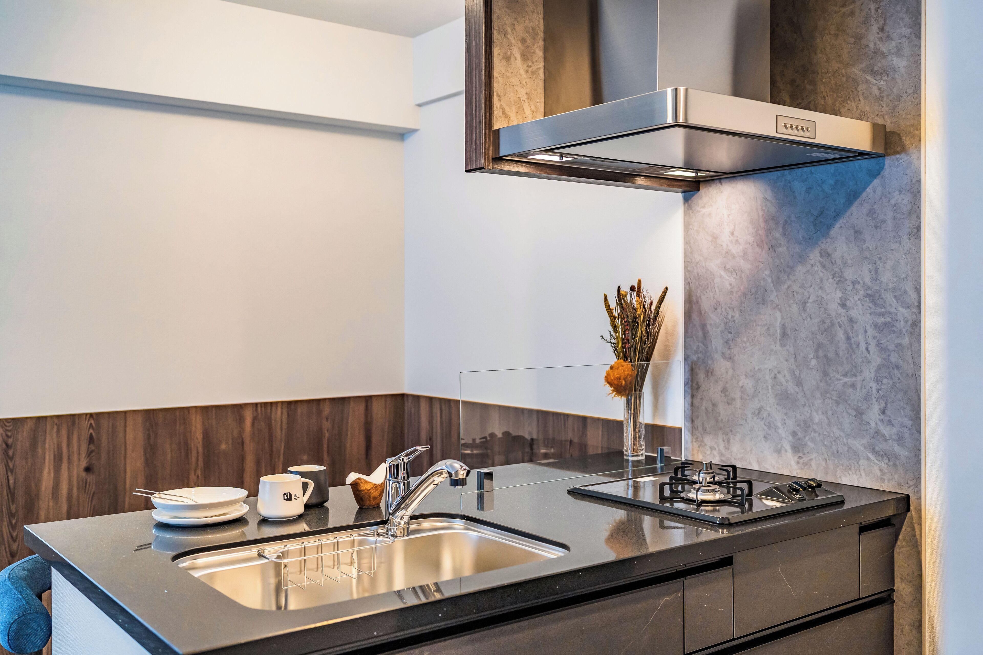 A modern kitchen with a stainless steel range hood, a double sink, and a vase with dried flowers on the counter.