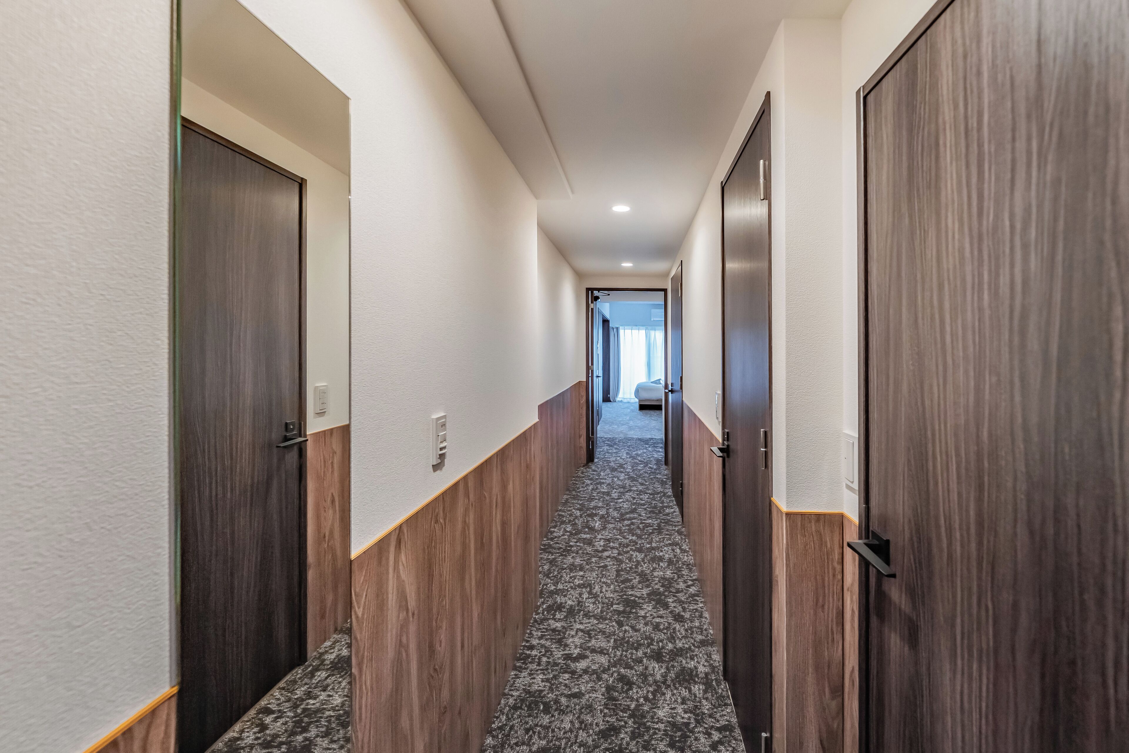 A hallway with wooden and white walls, carpeted floor, and doors leading to rooms.