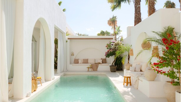 A poolside area with a seating area, white walls, and palm trees.