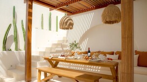 A sunlit dining area with a wooden table set for a meal, surrounded by white walls and featuring a cactus wall.