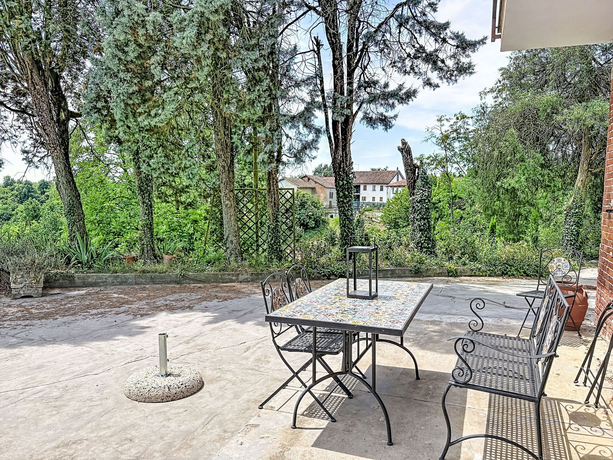 An outdoor patio with a metal table and chairs, surrounded by trees and a brick wall.