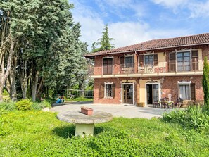 Un bâtiment en briques de deux étages, doté d’un balcon, un jardin avec une table en pierre circulaire et, au fond, une aire de jeux.