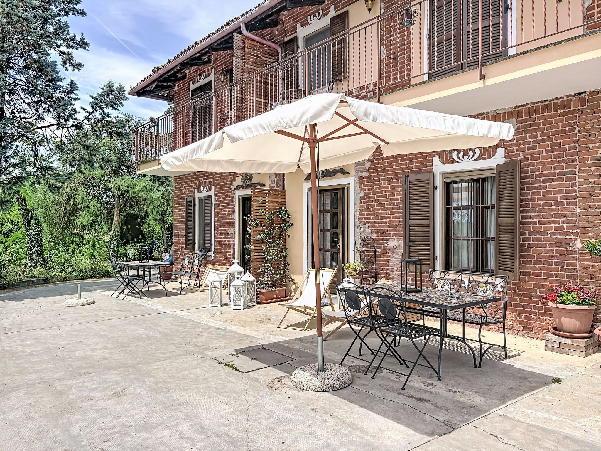 Un espace patio aménagé avec du mobilier d’extérieur, un parasol blanc et un bâtiment en briques doté de volets.