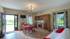 A spacious room with a dining area, kitchen, and a bed with red pillows.