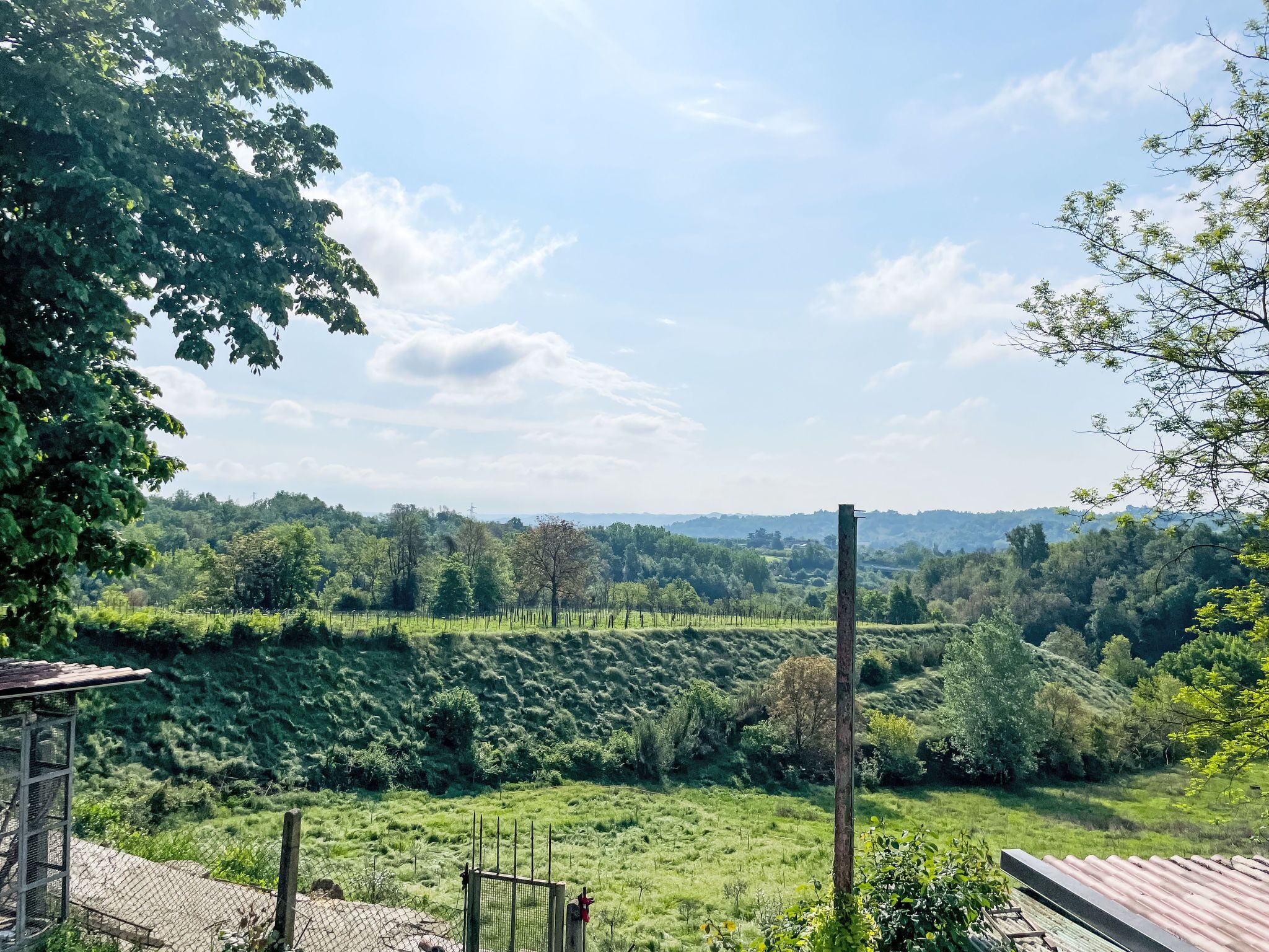 A rural landscape with a fenced field, a wooden post, and a metal structure.