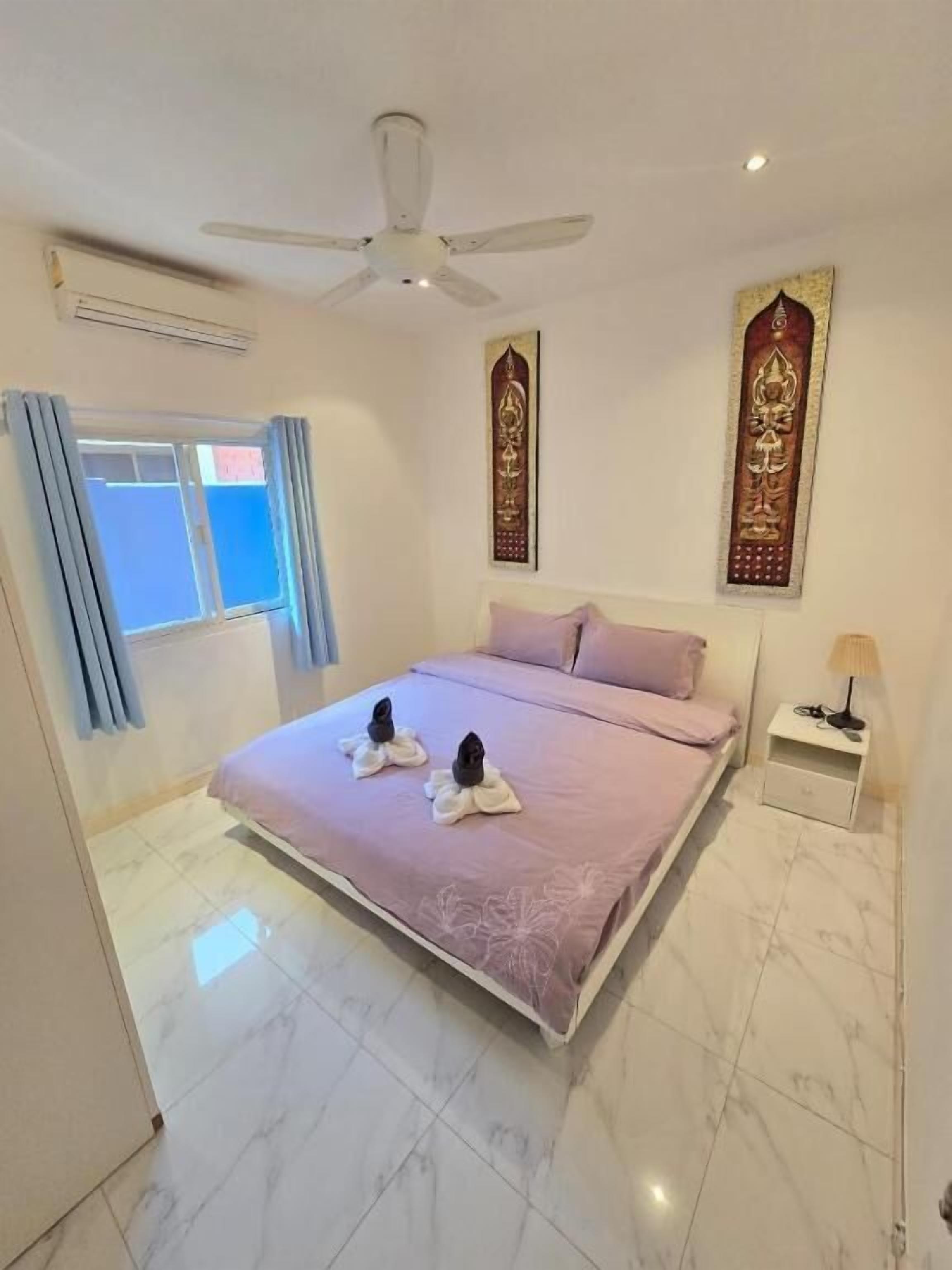 Een hotelkamer met een bed, een plafondventilator, een nachtkastje met lamp en decoratieve muurkunst.