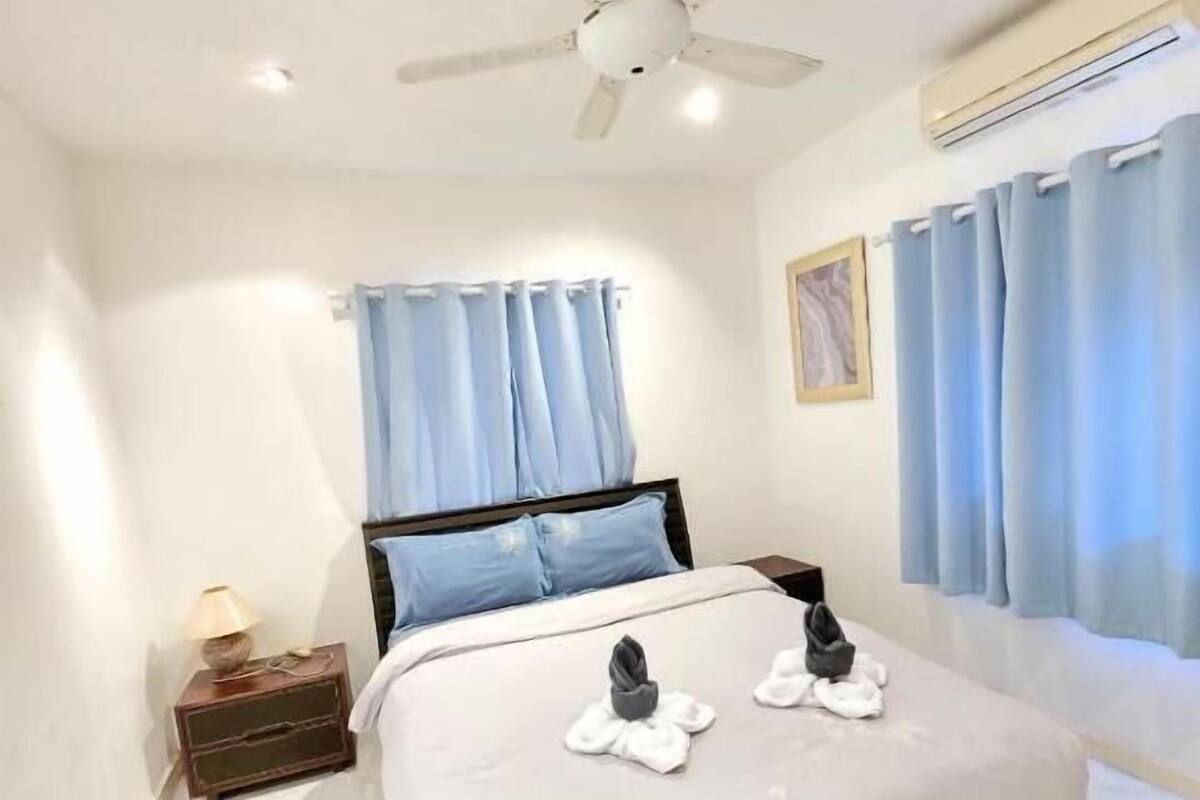 Ein Hotelzimmer mit einem Bett, einem Deckenventilator, einem Nachttisch mit Lampe und einem Fenster mit Vorhängen.