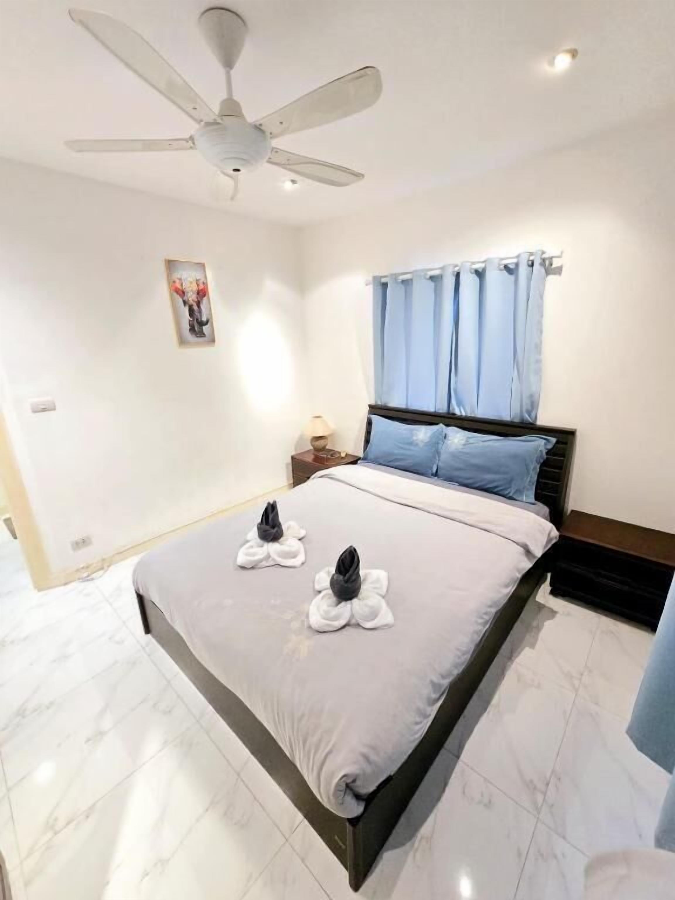 A hotel room with a bed, a ceiling fan, a nightstand, and a window with curtains.