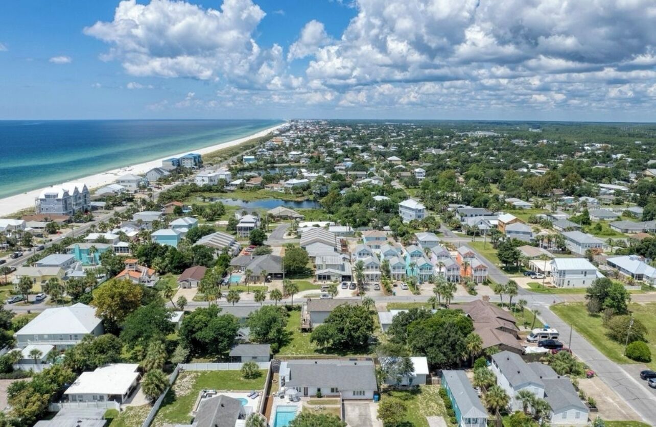 An aerial view of a coastal residential area with houses, a beach, and a clear sky.