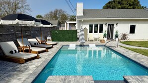 A swimming pool with lounge chairs and umbrellas, a small deck area, and a house in the background. - Quiet Laguna Beach Home- 1  Block to Ocean - Pool & Spa-Pets - Games - Sleeps 14 (Panama City Beach)