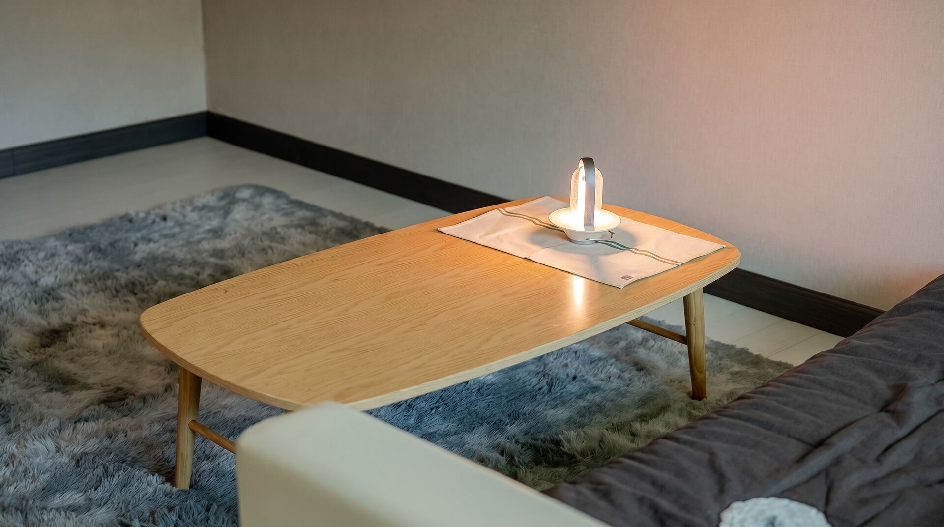A small wooden table with a lamp on it, placed on a fluffy rug in a room with a sofa.