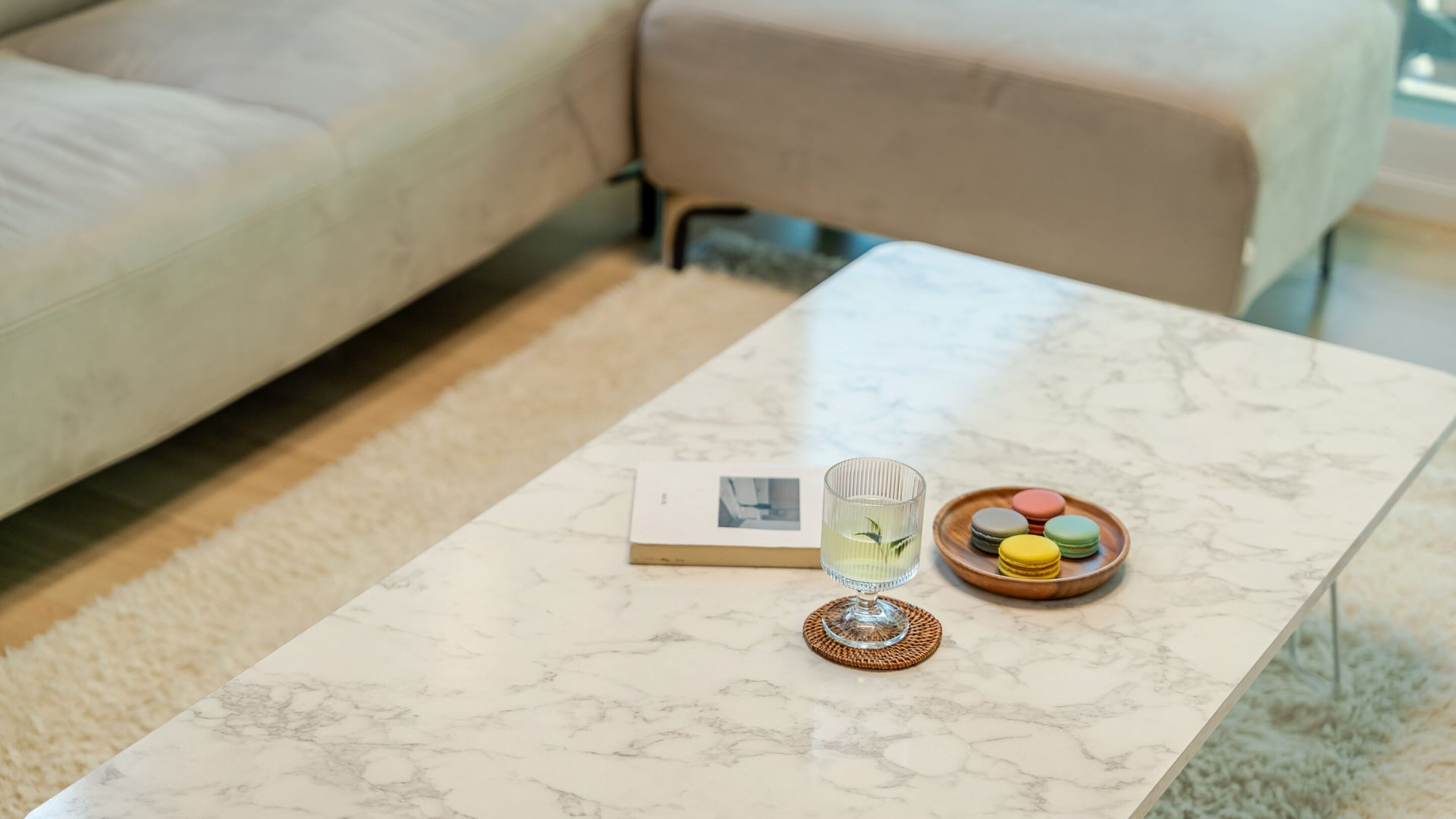 Une table basse en marbre sur laquelle sont posés un livre, un verre d’eau et une assiette de macarons multicolores.