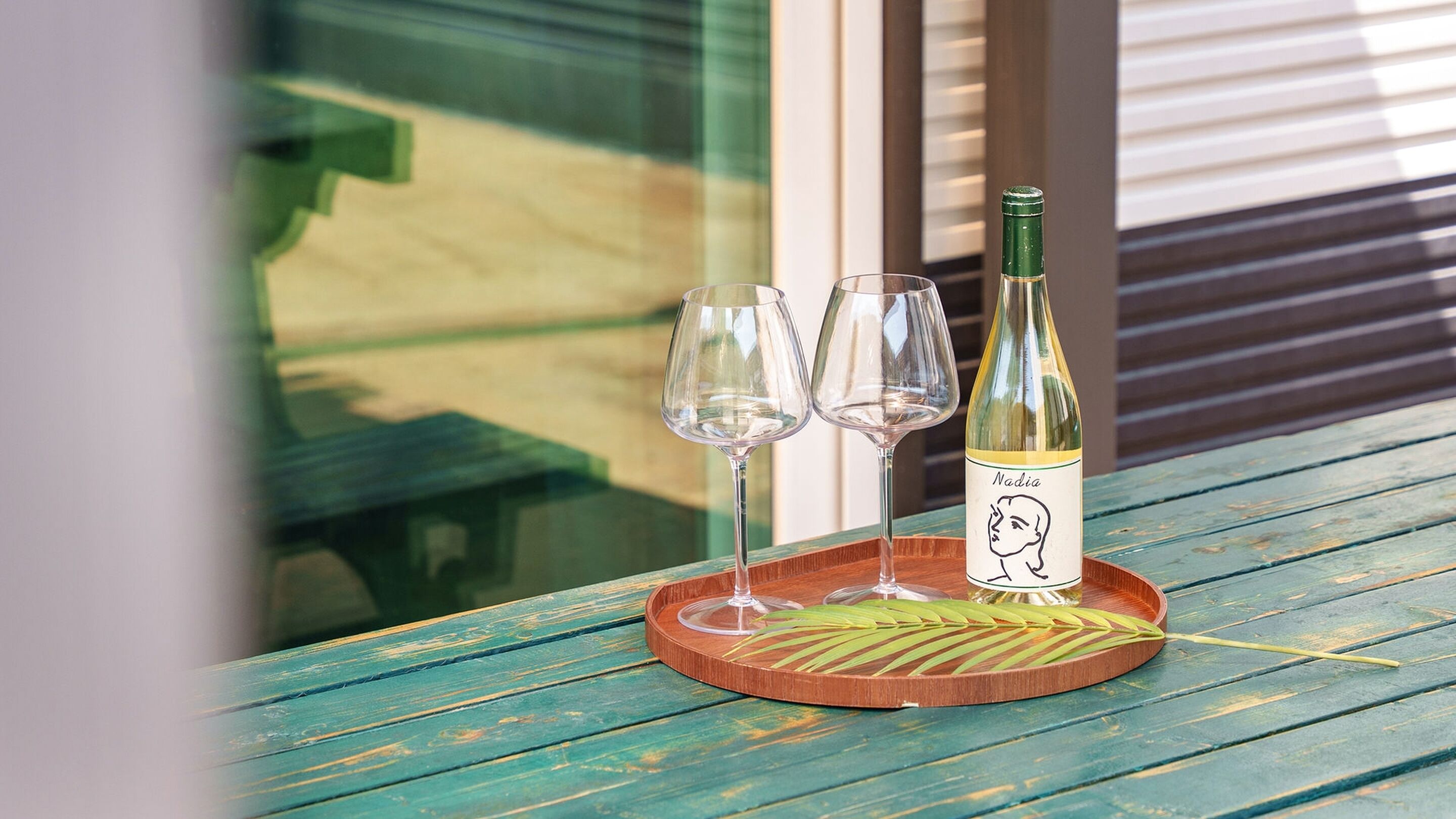 A bottle of wine and two glasses on a wooden tray on a table.