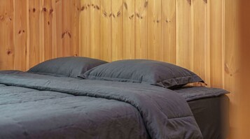Una cama con edredón gris y almohadas frente a una pared de madera.