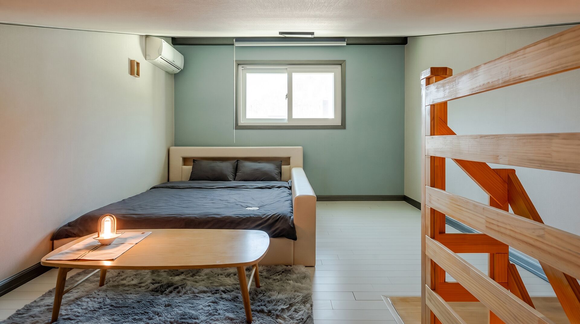 Une chambre à coucher avec un lit, une petite table, une fenêtre et une rambarde en bois.