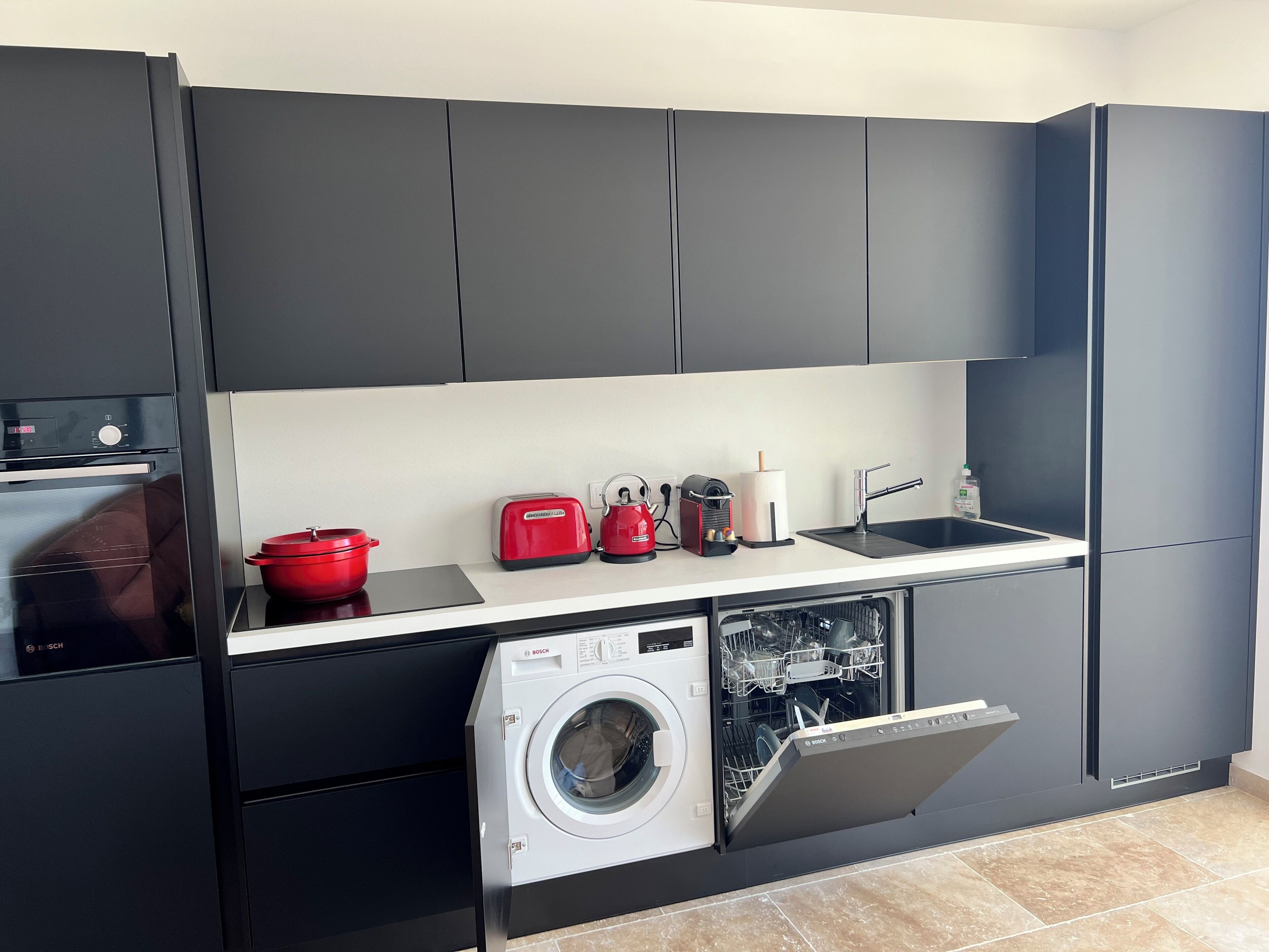 A modern kitchen with a Bosch dishwasher, a red pot, a toaster, and a sink.