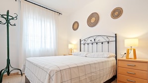 Une chambre à coucher avec un lit, deux tables de chevet avec des lampes, une petite table en bois, un tapis à motifs et un lampadaire vert.