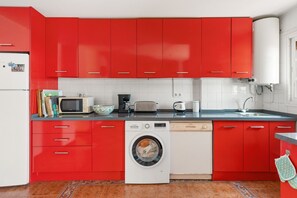 Een keuken met rode kastjes, een wasmachine, een magnetron, een broodrooster en een spoelbak.