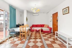 Quarto com mesa de jantar, cadeiras, sofá vermelho, piso estampado, candelabro e porta com telefone.