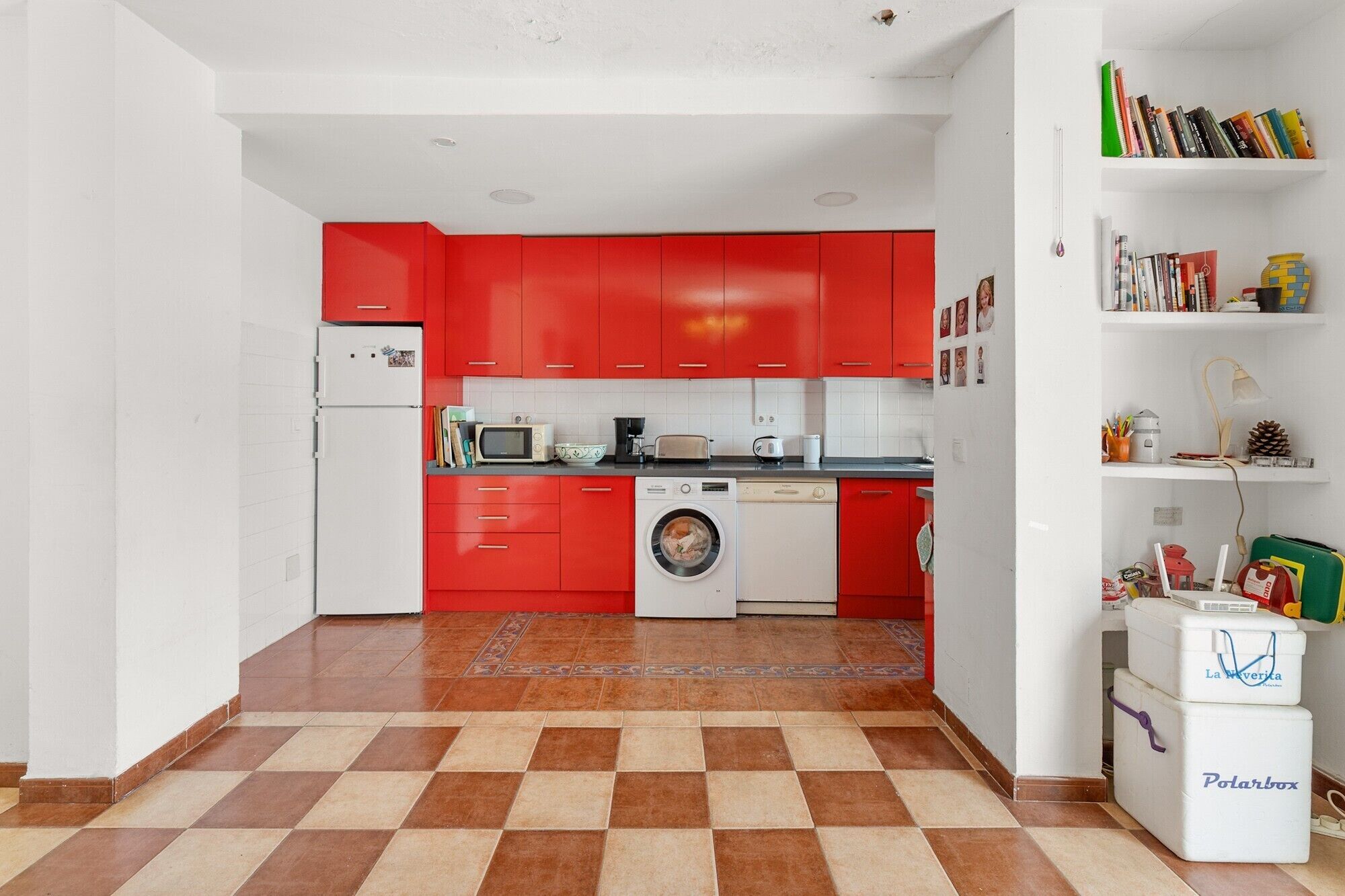 Cocina pequeña con armarios rojos, lavadora, microondas y refrigerador.