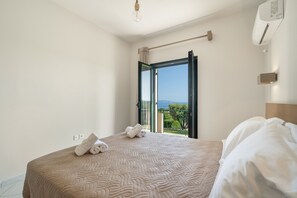 Une chambre avec un lit, une serviette, une porte ouverte donnant sur un balcon et un luminaire au plafond.