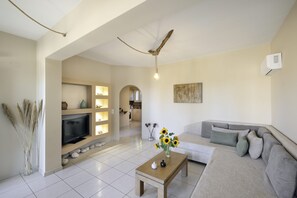 Un salon comprenant un canapé, une table basse avec un vase, un téléviseur à écran plat et un ventilateur de plafond.