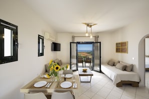 A dining area with a table set for two, a sofa, a TV mounted on the wall, and a view through a glass door.