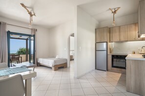 Une cuisine moderne équipée d’un réfrigérateur, d’un four et de meubles de rangement en bois. La pièce comprend également une table à manger avec des chaises et un petit lit.
