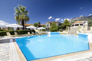 Une piscine entourée de bâtiments et d’un palmier, avec des chaises longues et des parasols.