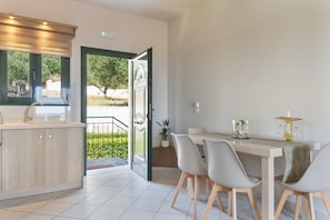 A modern kitchen with a dining area, a view of greenery outside, and a door leading to an outdoor space.