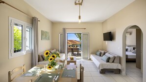 Ein Zimmer mit Esstisch, Stühlen, einer Couch und einem an der Wand befestigten Fernseher.