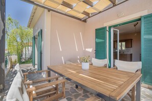 Una mesa de madera con sillas, una planta en maceta y vistas a una cocina a través de una puerta abierta.