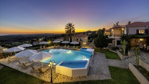 Ein Pool mit Liegestühlen und Sonnenschirmen, umgeben von Steinwegen und Grünpflanzen.