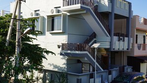 Ein mehrgeschossiges Gebäude mit einer Treppe, die zu den oberen Stockwerken führt, ein geparktes Auto und ein Strommast mit Leitungen.
