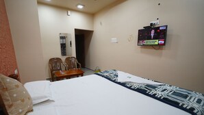 Ein Hotelzimmer mit einem Bett, einem Schreibtisch, zwei Stühlen, einem Fernseher und einer Tür zu einem weiteren Raum.