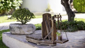 A rustic outdoor water pump with a wooden structure, a stone base, and a potted plant. - Villa Ersime with Sea View (Mousata)