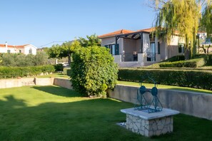 Un quartiere residenziale con un prato curato, una panchina in pietra e una casa con tetto rosso.