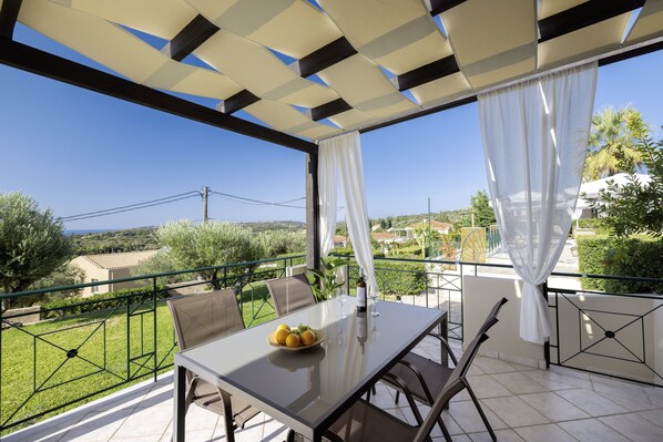 A balcony with a table, chairs, and a bowl of fruit.