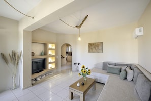 A living room with a sofa, a coffee table with a vase, a flat-screen TV, and a ceiling fan.