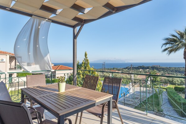 Una terraza con mesa y sillas, vista al mar y una piscina.