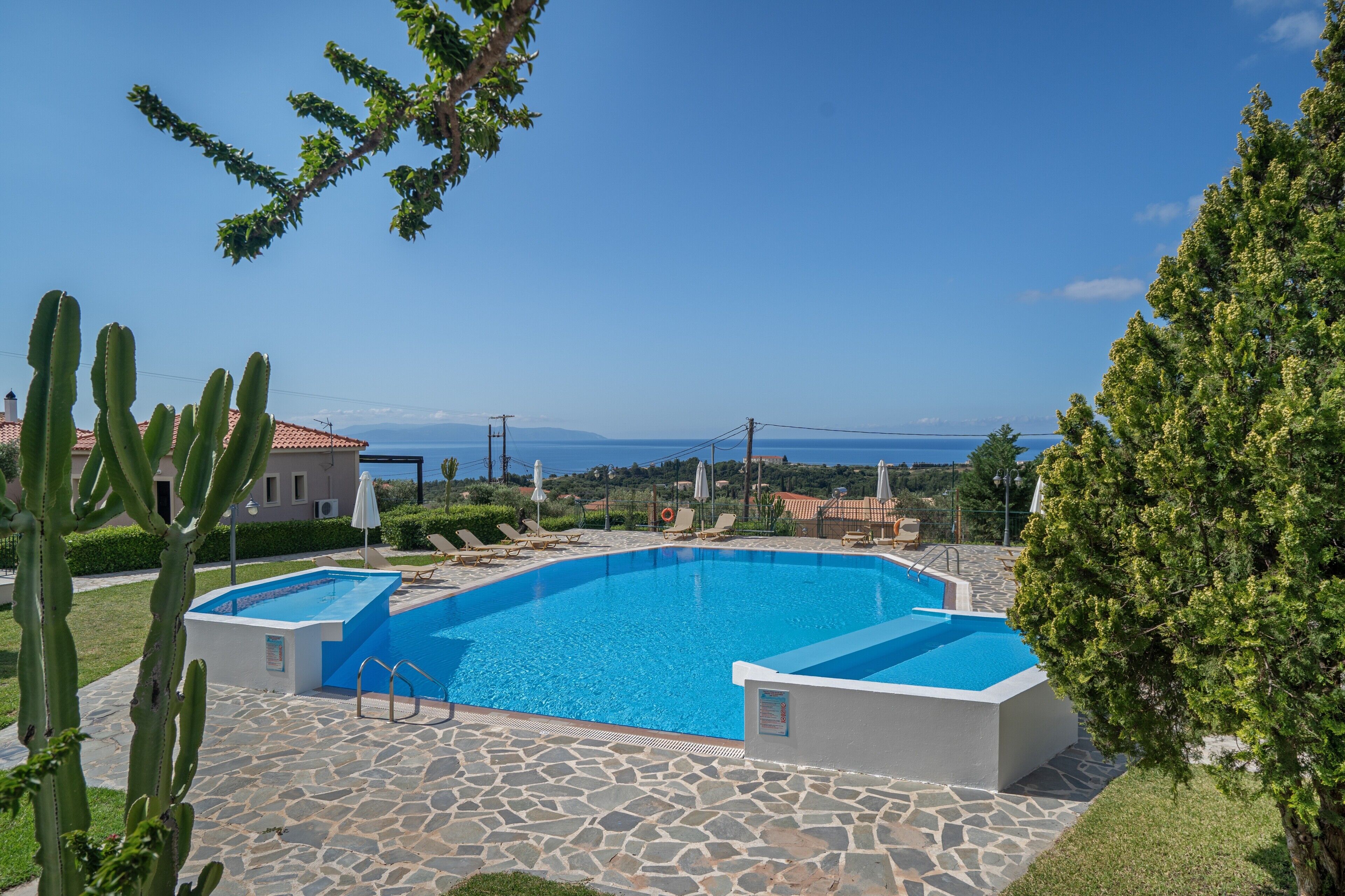 Une piscine avec une terrasse en pierre, entourée de verdure et offrant une vue sur la mer.