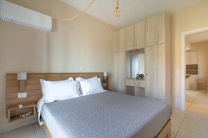 Une chambre à coucher comprenant un lit, des tables de chevet, une commode, une armoire, un miroir et un coin cuisine.