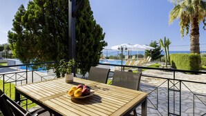 Una mesa de madera con un frutero, asientos al aire libre, vista a la piscina y una palmera.