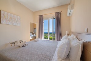 Une chambre d’hôtel avec un lit, une vue sur la mer, une fenêtre avec des rideaux et un porte-serviettes.