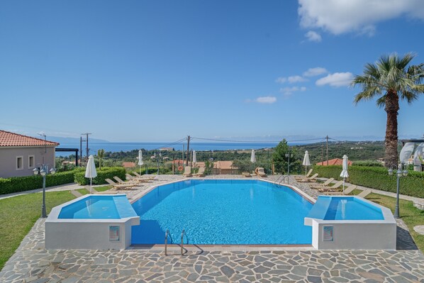 A swimming pool with a view of the sea, surrounded by lounge chairs and umbrellas.