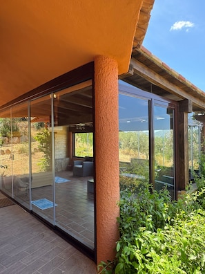 Une terrasse extérieure moderne, dotée de portes vitrées, d’un plafond en bois et offrant une vue sur un jardin.