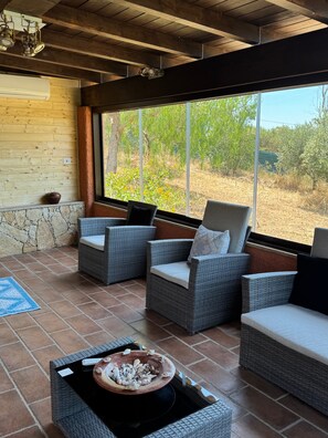 A patio area with wicker furniture, a stone wall, and a view of a garden.