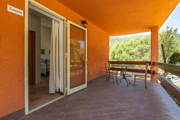 A covered patio with a table and chairs, a sliding glass door leading to a room, and a sign reading 'Campus'.