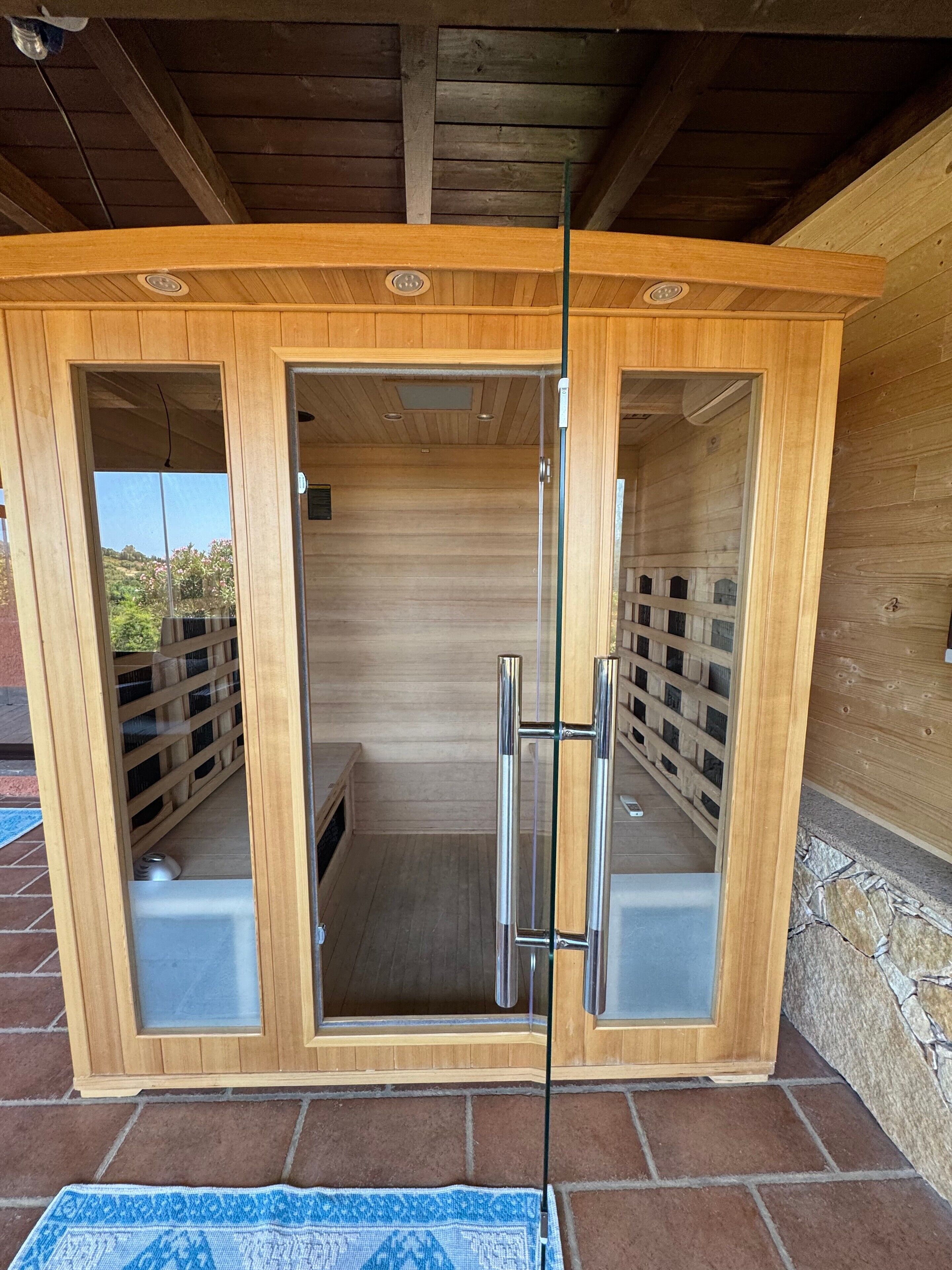 A wooden sauna with a glass door, a metal handle, and a tiled floor.